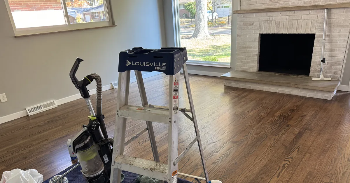 Living room with a brick fireplace and hardwood floors, with a ladder and cleaning equipment staged for a house cleaning in St. Louis