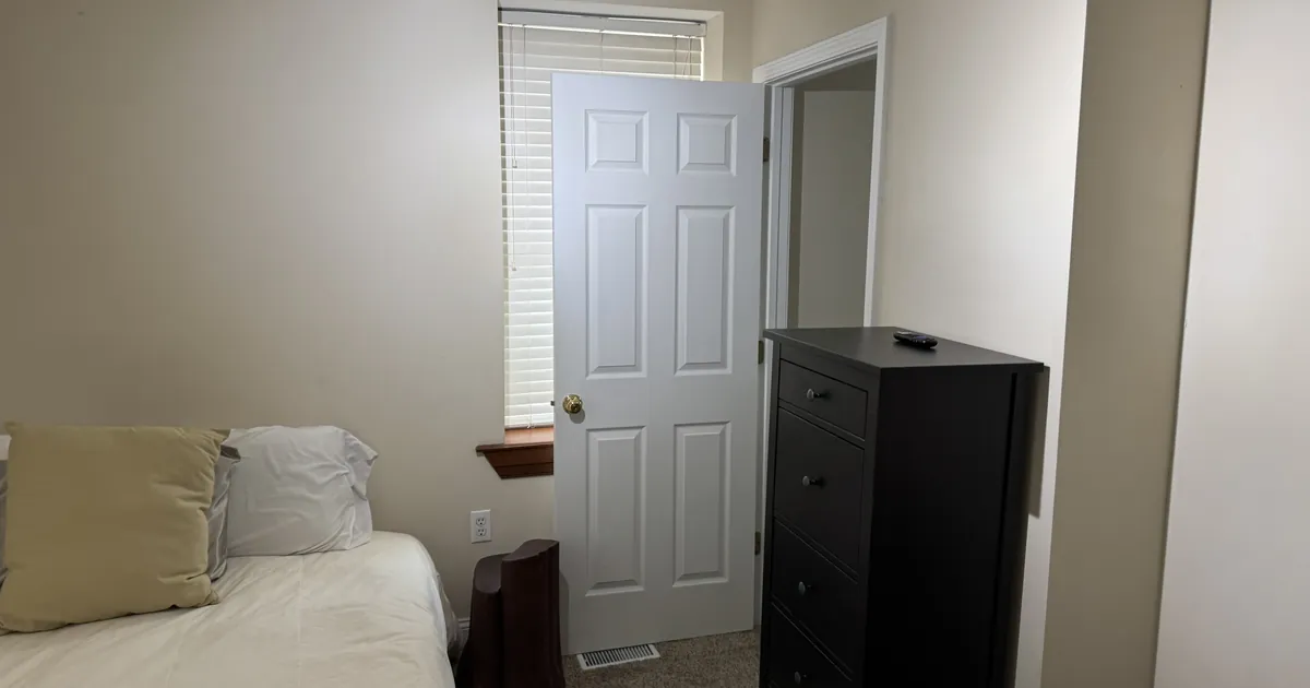 Neat bedroom with a made bed and dark wood dresser after a home cleaning in St. Louis