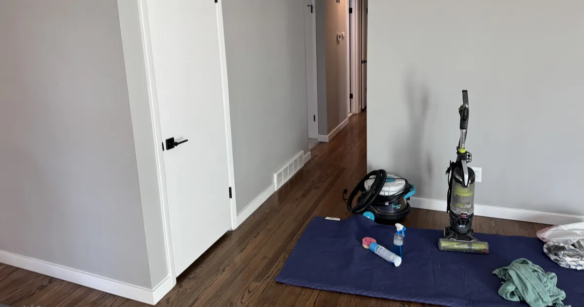 Hallway with white baseboards and hardwood floors, with cleaning equipment on a protective mat