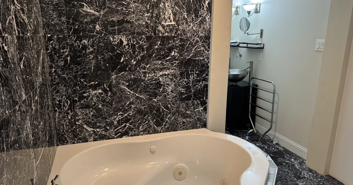 Bathroom with a jetted tub, black marble-look tile and a vanity mirror with wall sconces