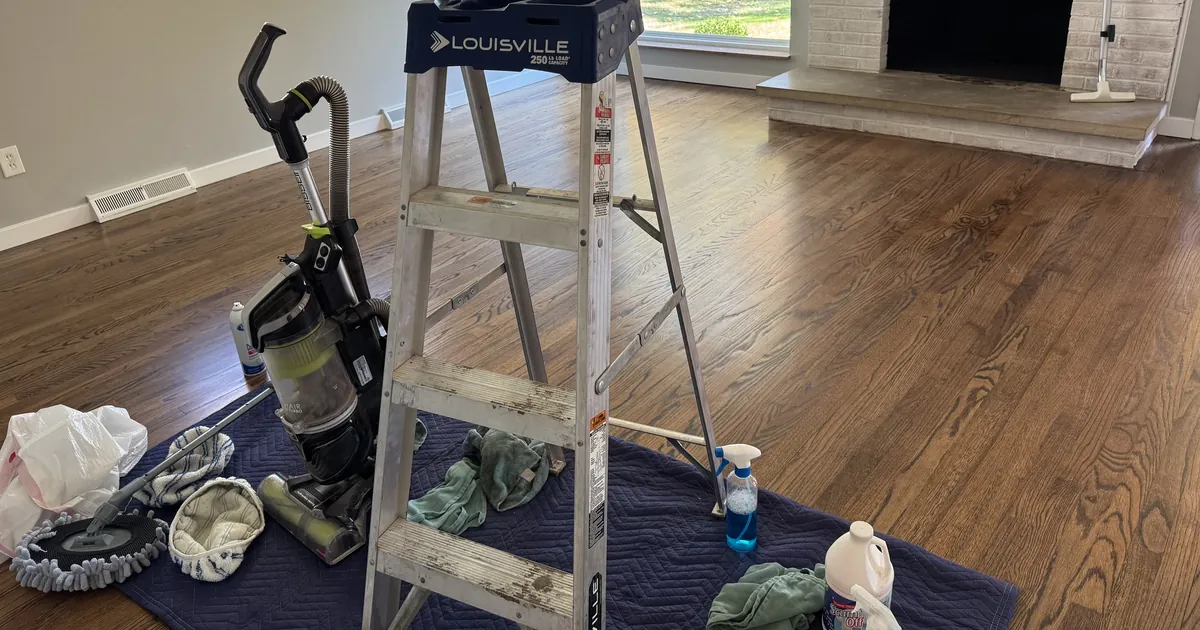 Refinished hardwood floor with a ladder, vacuum and supplies on a protective mat during a post-construction clean