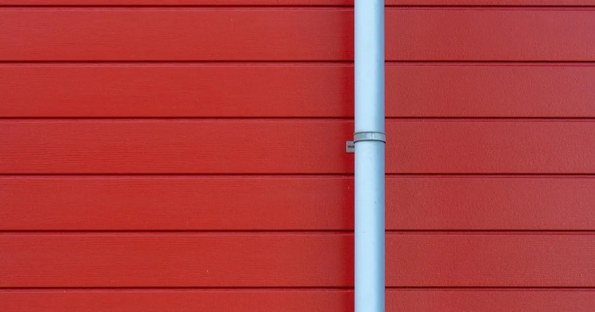 White gutter downspout running down red house siding